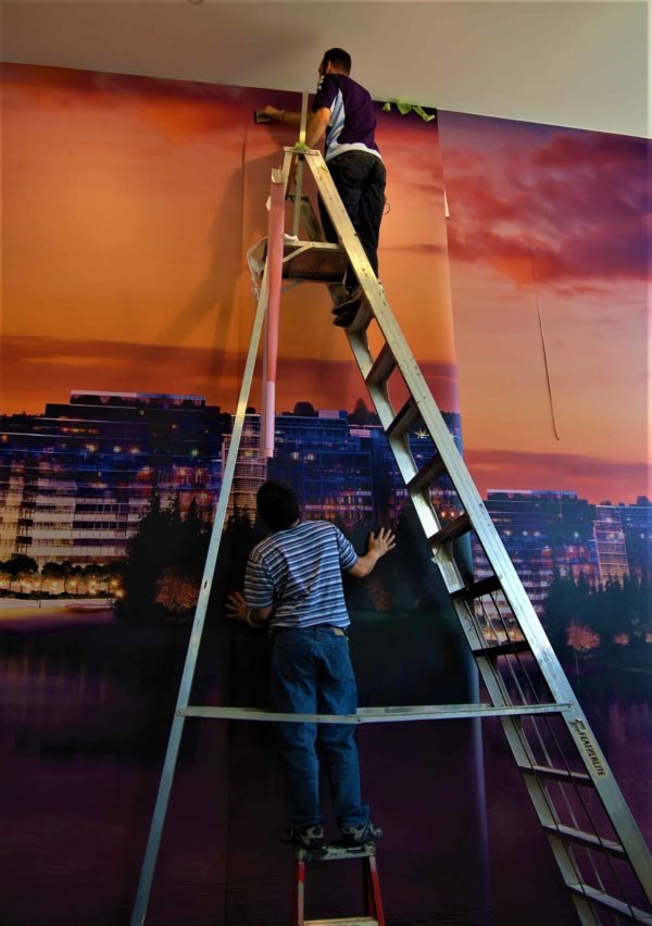 Two T.K. Graphics installers mounting a large city skyline mural graphic